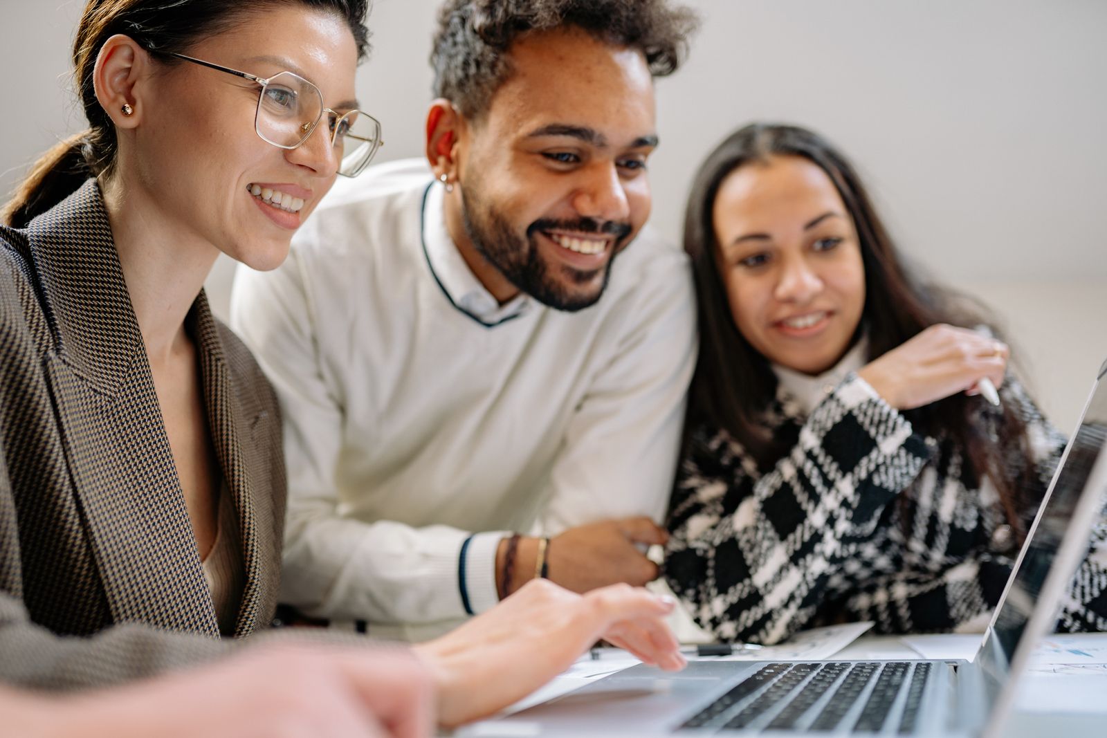 Three colleagues smiling while reviewing keyword research on a laptop