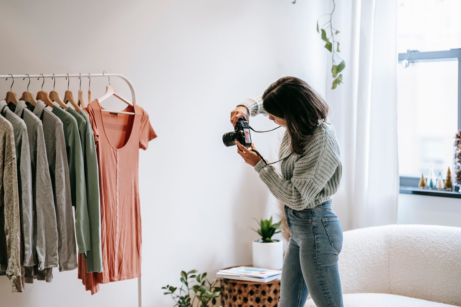 A photographer taking a picture of clothes displayed on hangers beside a bright window
