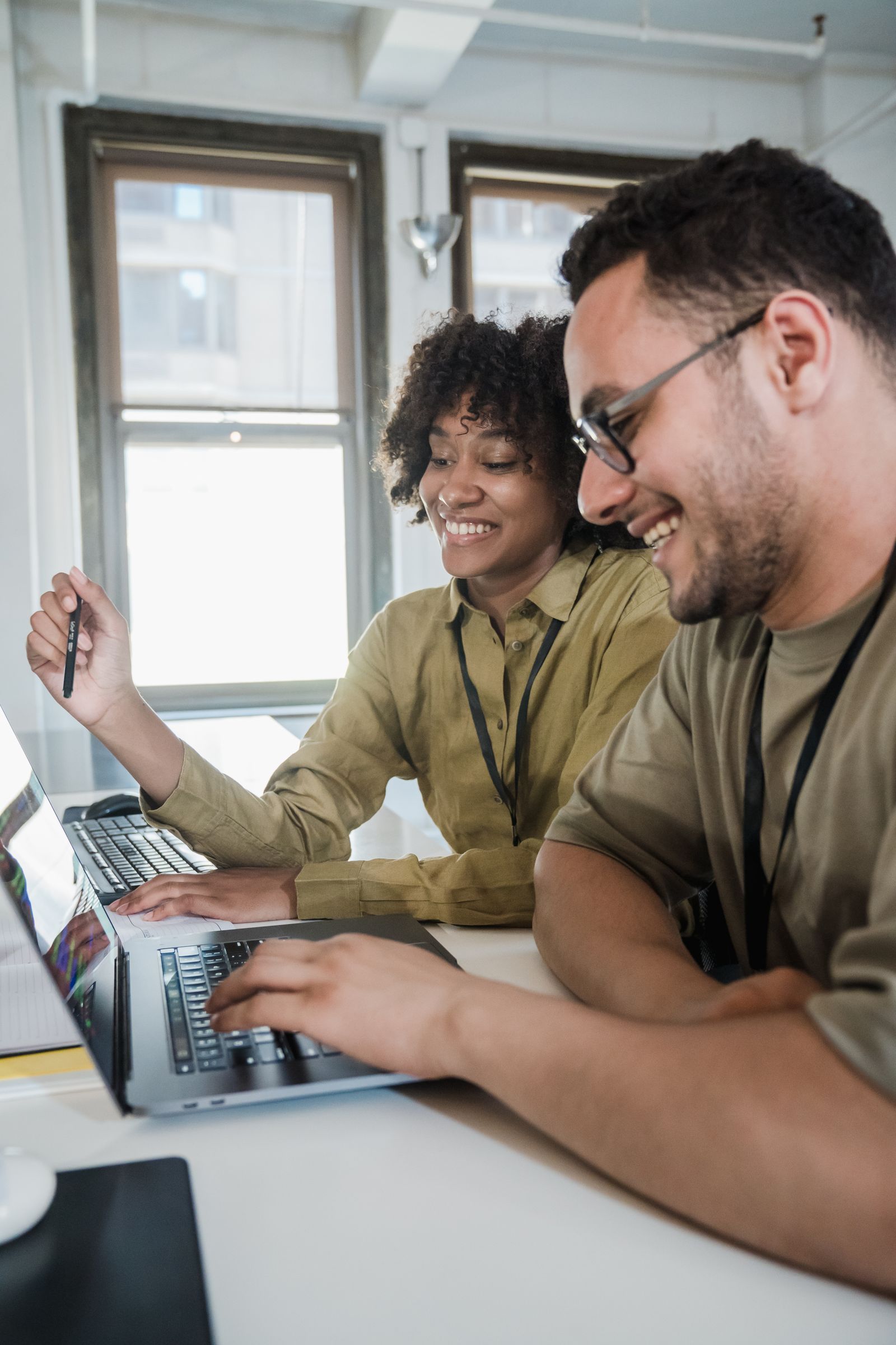 Two colleagues smiling while reviewing listing information on laptops